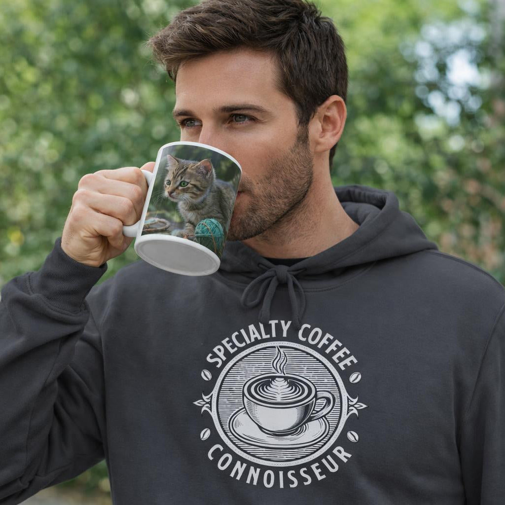 Man wearing a hoodie with 'Specialty Coffee Connoisseur' design, holding a mug outdoors.