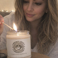 Woman lighting a candle labeled 'Christmas Warmth' with a match.