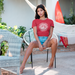 Woman in a red Specialty Coffee Connoisseur t-shirt sitting on a chair outdoors with plants and a hammock in the background.