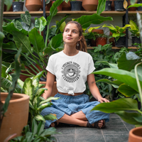 Woman sitting among plants wearing a white t-shirt with a coffee graphic.